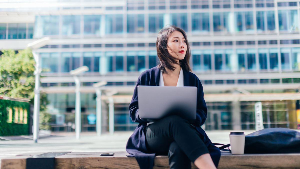 A woman holding a laptop sat outside an office building during the day