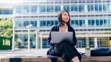 A woman holding a laptop sat outside an office building during the day