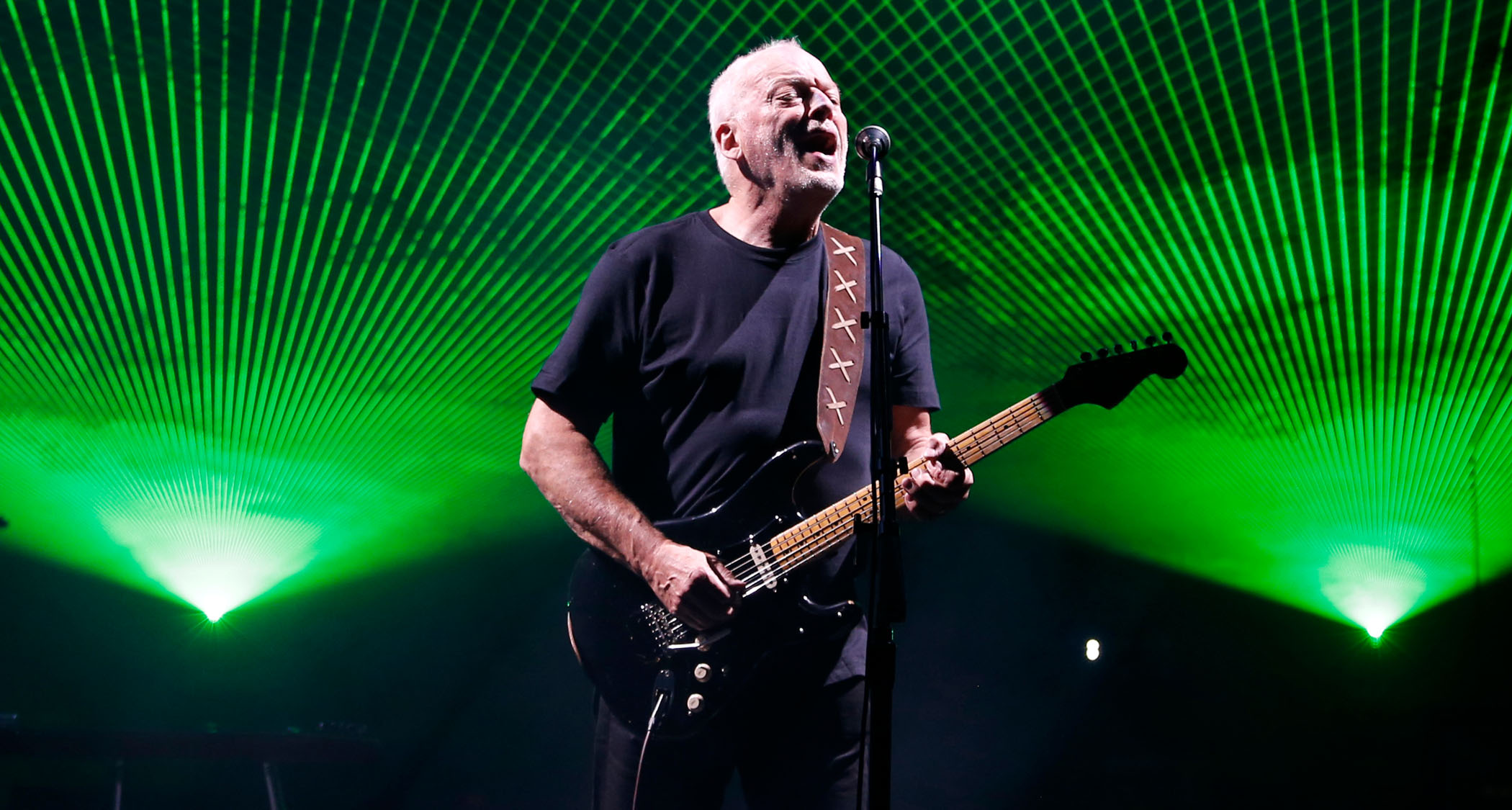 David Gilmour performs with a black Stratocaster as green lasers are fanned out above his head.