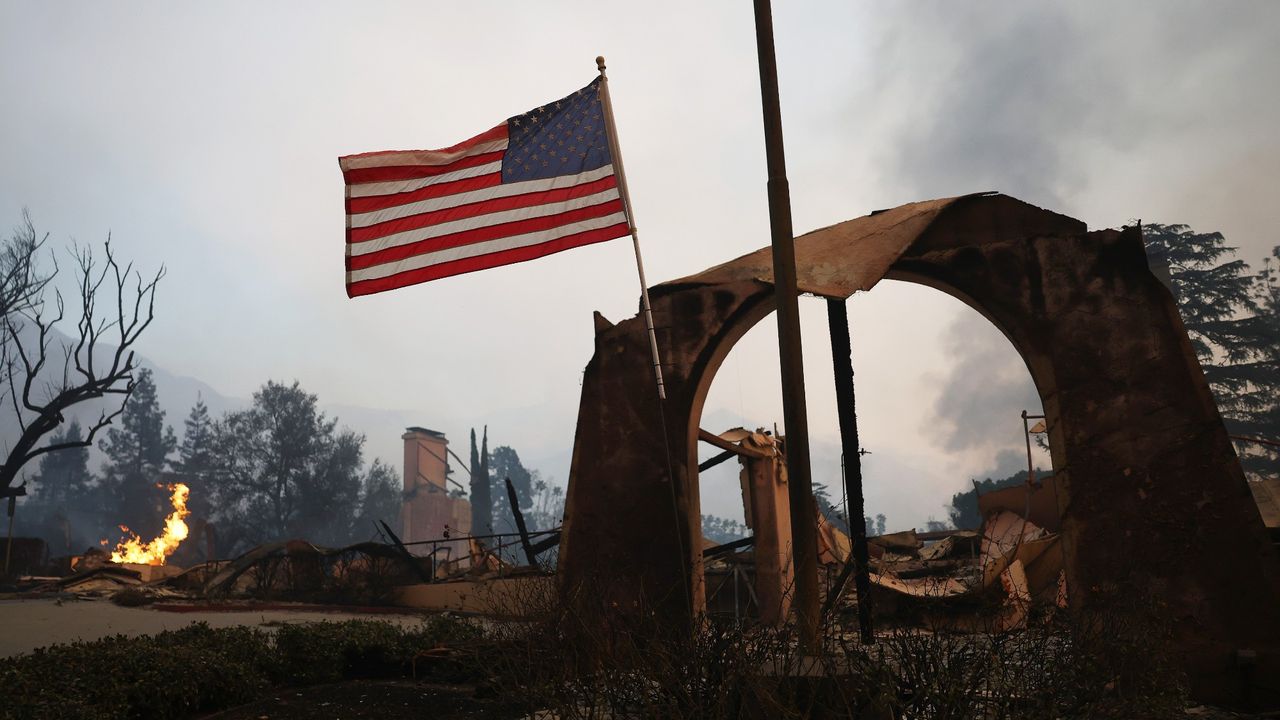 An American flag flies amid burned structures at the Altadena Town &amp; Country Club during the Eaton Fire on January 8, 2025 in Altadena, California