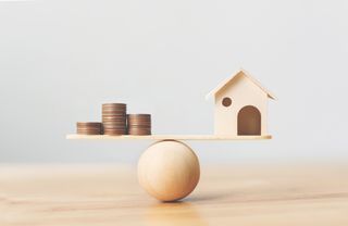 rendering of wooden house balanced on a scale with coins