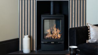 A lit log burner in a vertical stripe tiled surround 