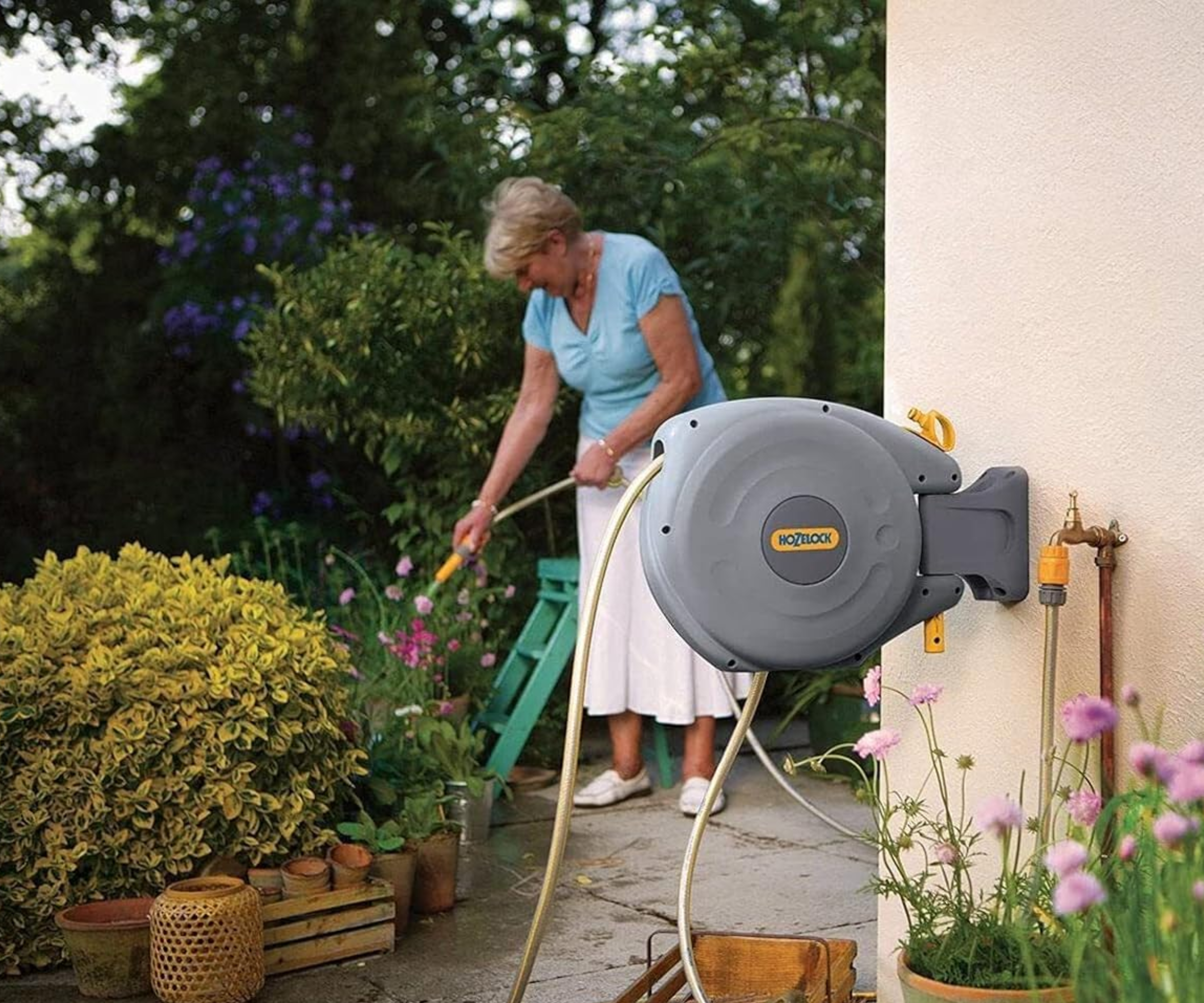 wall mounted hose in garden with woman in background using it