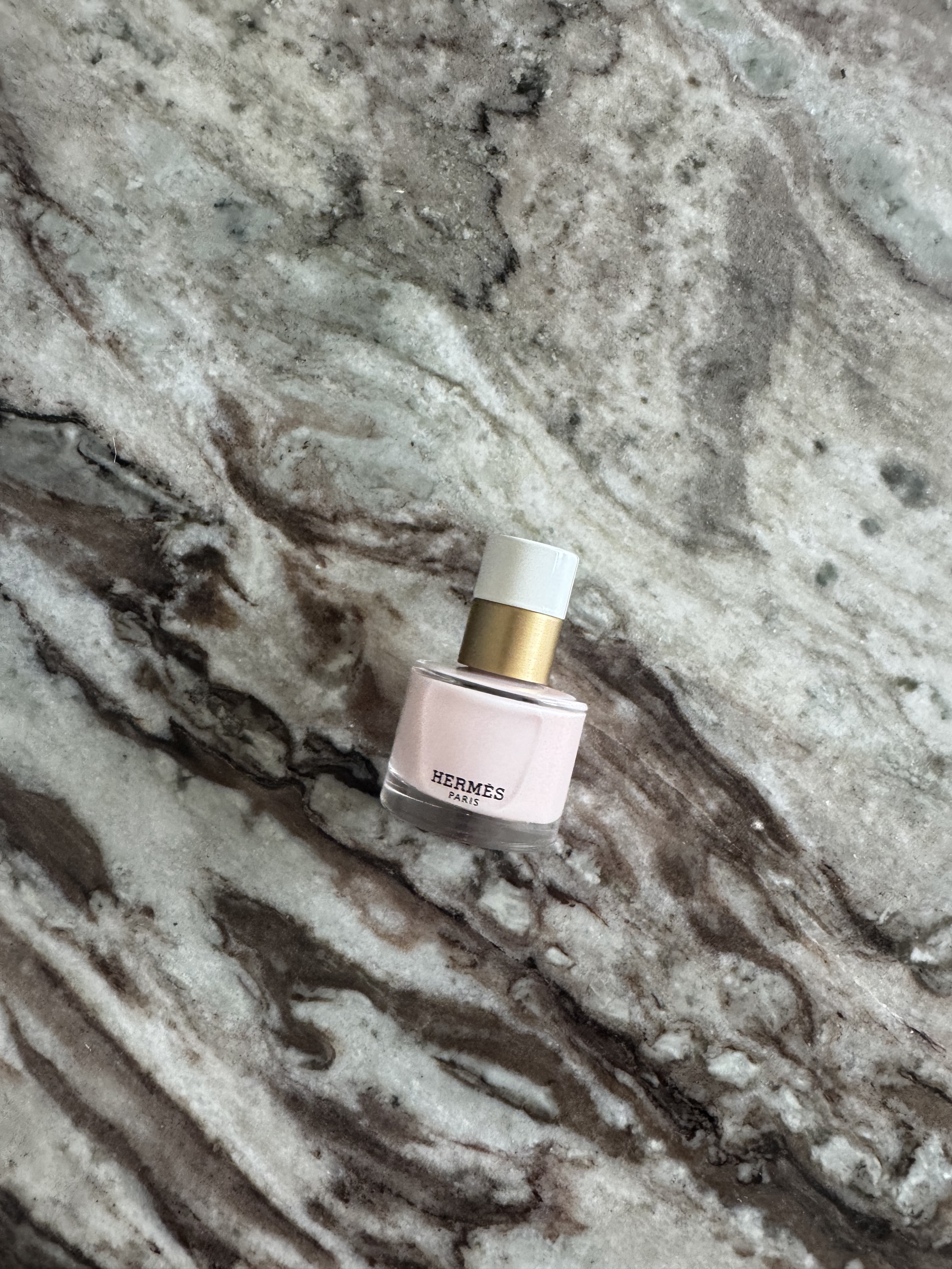 A bottle of Hermes Les Mains Hermes Nail polish in Rose Porcelaine on a marble table
