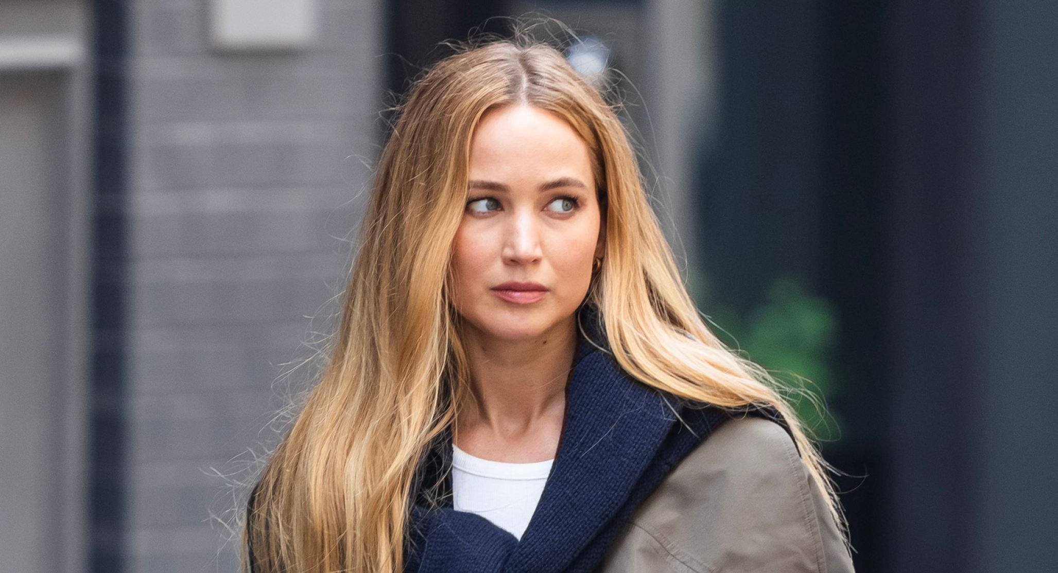 Jennifer Lawrence has long blonde hair and wears a navy sweater tied around her shoulders in SoHo on June 28, 2023 in New York City