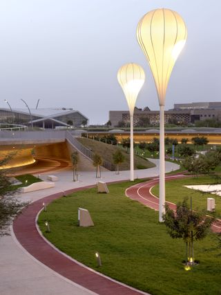 Qatar’s Oxygen Park, curved grass and concrete pathways, framed by ground and tall balloon shaped lights, sculpturally designed landscape with trees and grass verges, with buildings in the distance against a grey sky