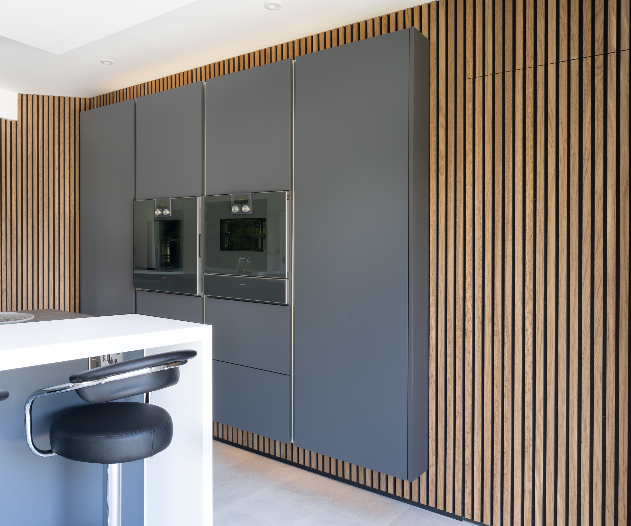 kitchen with wall panelled wall and grey units with built in appliances in centre