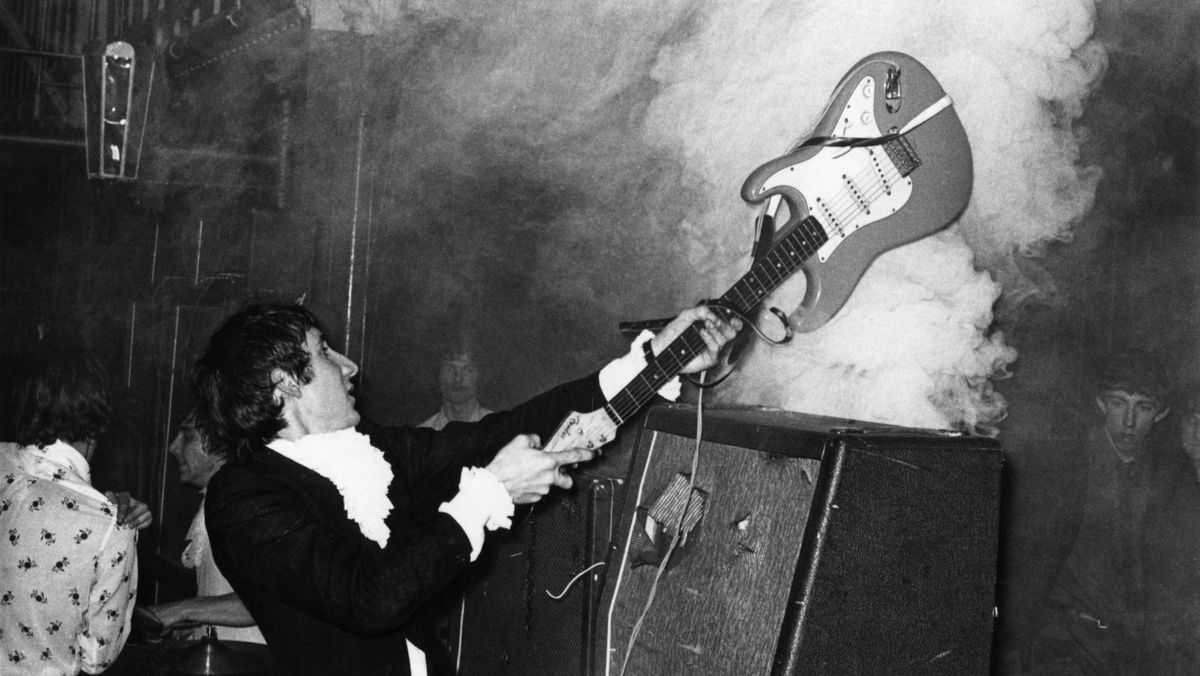 Pete Townshend performing live onstage, smashing guitar against amplifier 