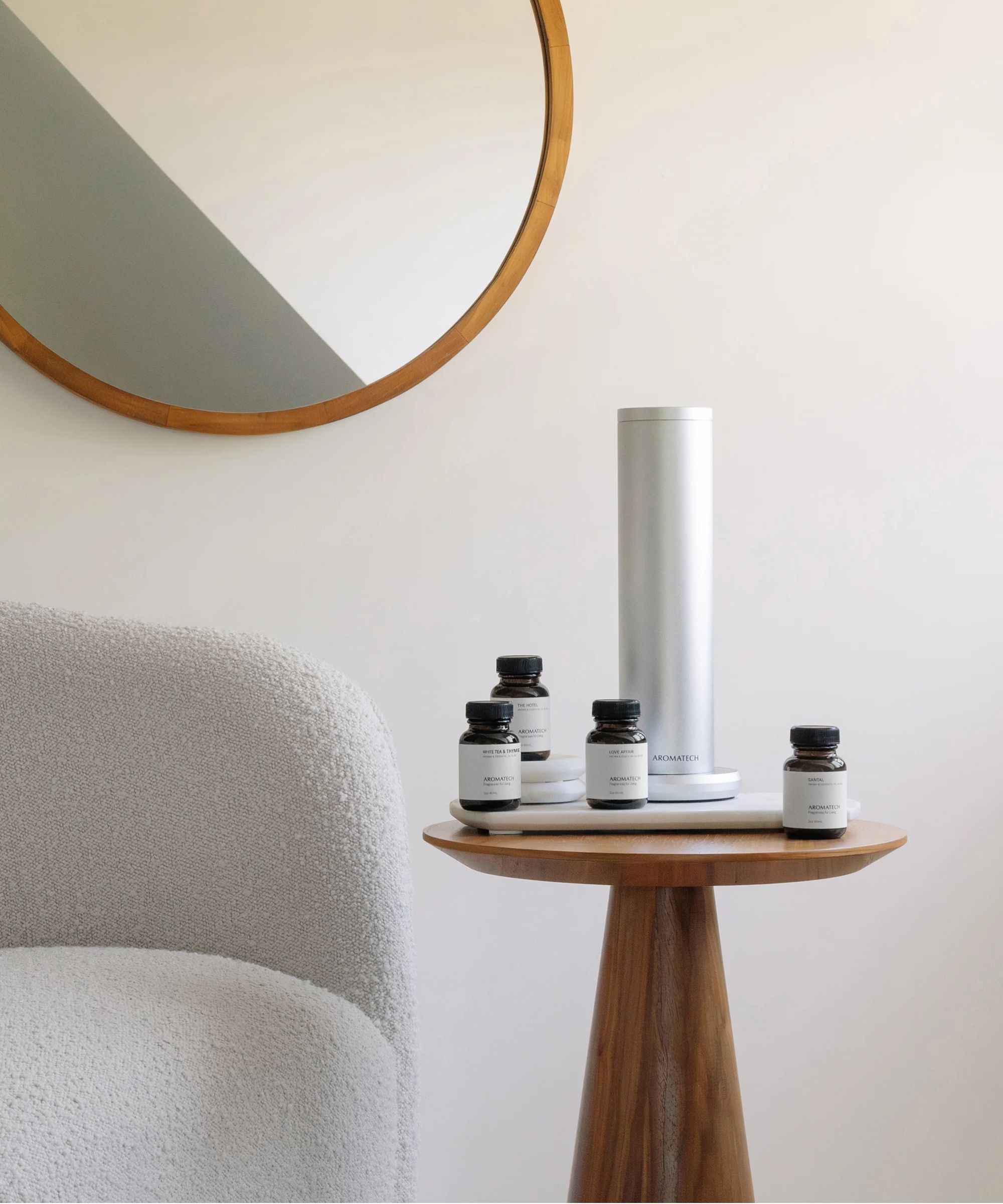 AromaTech AroMini on a wooden table with a boucle chair and circular mirror against a white wall.