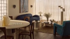 living room with sheer curtains, glass breeze blocks, round table with dark wood chairs, blue sofa, with blue armchair, with steel coffee table with beige rug and floor lamp