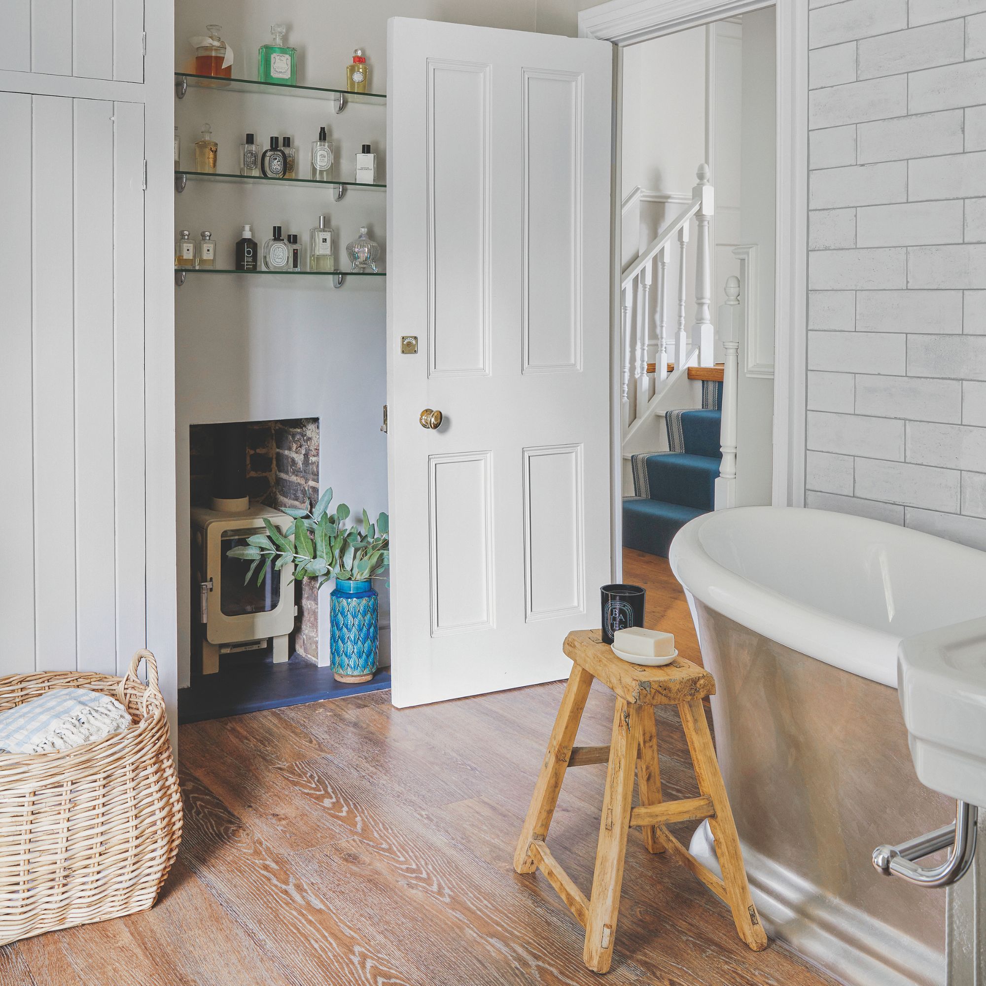 White bathroom with wooden floor and a freestanding bath, and a basket filled with blankets on the floor