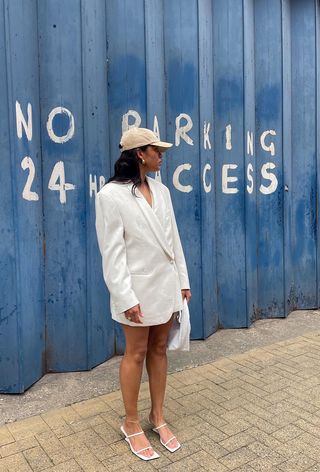 A woman's white dress outfit styled with a baseball cap and white sandals.