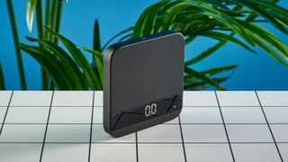 the acaia lunar coffee scale in black with an aluminum surface and accurate precise weight ideal for espresso machines given its compact size is photographed againt a blue tom's guide background