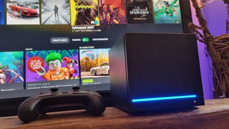 A Steam Machine in front of a TV next to a Steam Controller, showing the SteamOS in the background
