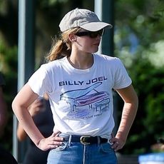 Jennifer Lawrence wearing a hat, white Billy Joel T-shirt, wide-leg jeans, and Vans sneakers.