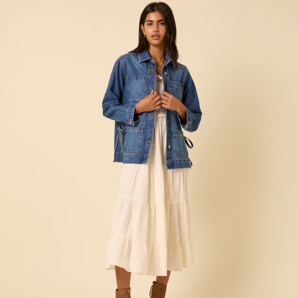 A model wearing a denim jacket and cream dress