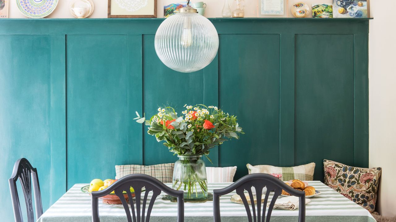 A dining room with teal-painted wall panelling, a sphere-shaped glass pendant light and a rectangular dining table