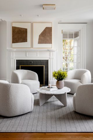 White living room with curved white boucle armchairs, light grey herringbone patterned rug, and abstract artwork with brown tones