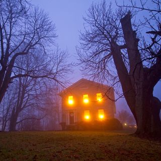 Creepy house in the woods at dusk with all lights on