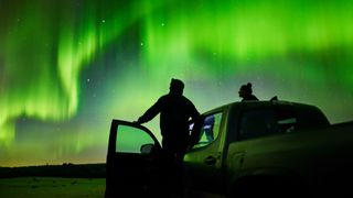 two people standing with a car looking at the northern lights above.