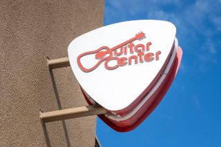 Close-up of pick-shaped logo sign at Guitar Center store in Emeryville, California with logo visible and blue sky behind