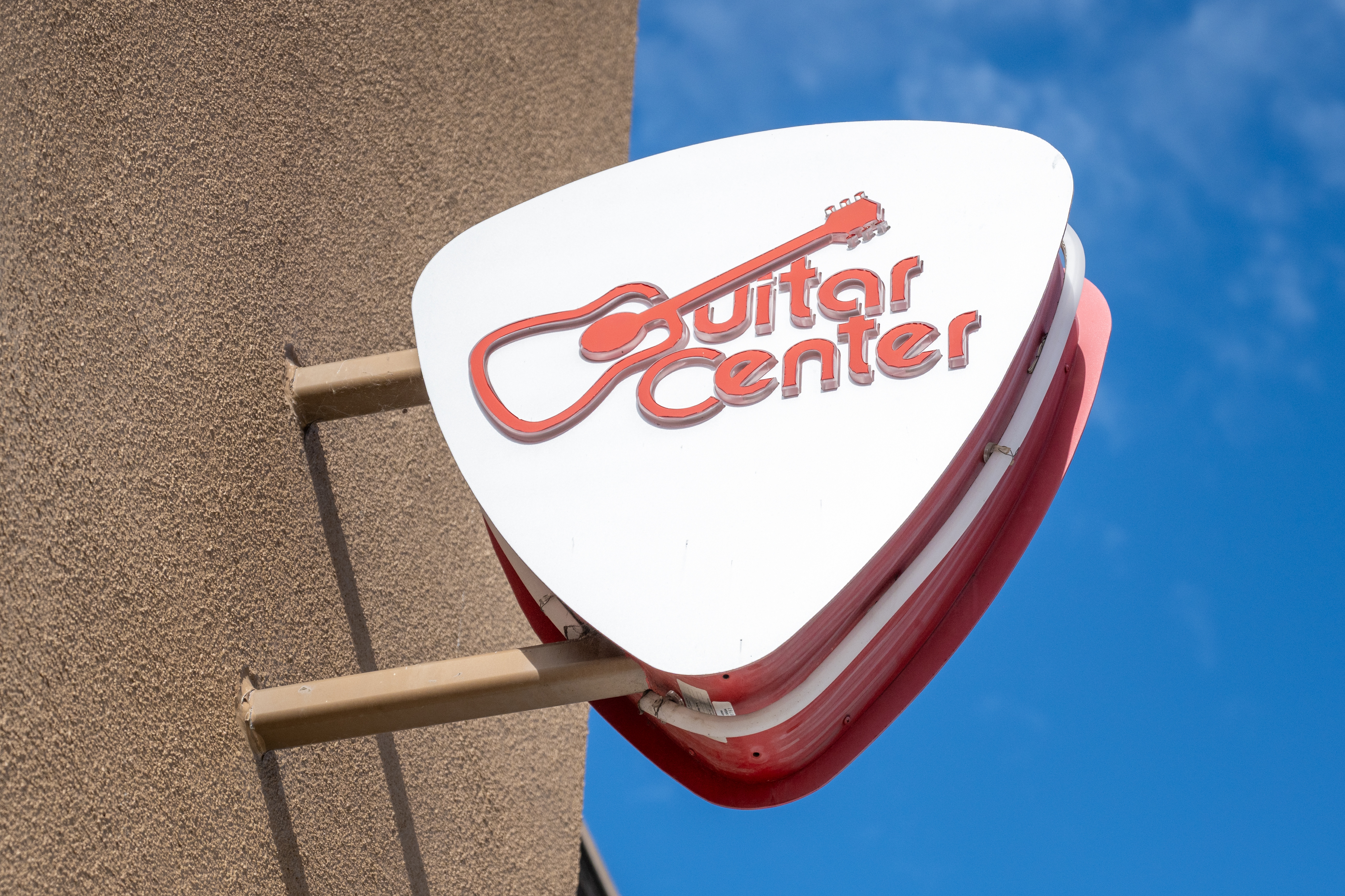Close-up of pick-shaped logo sign at Guitar Center store in Emeryville, California with logo visible and blue sky behind
