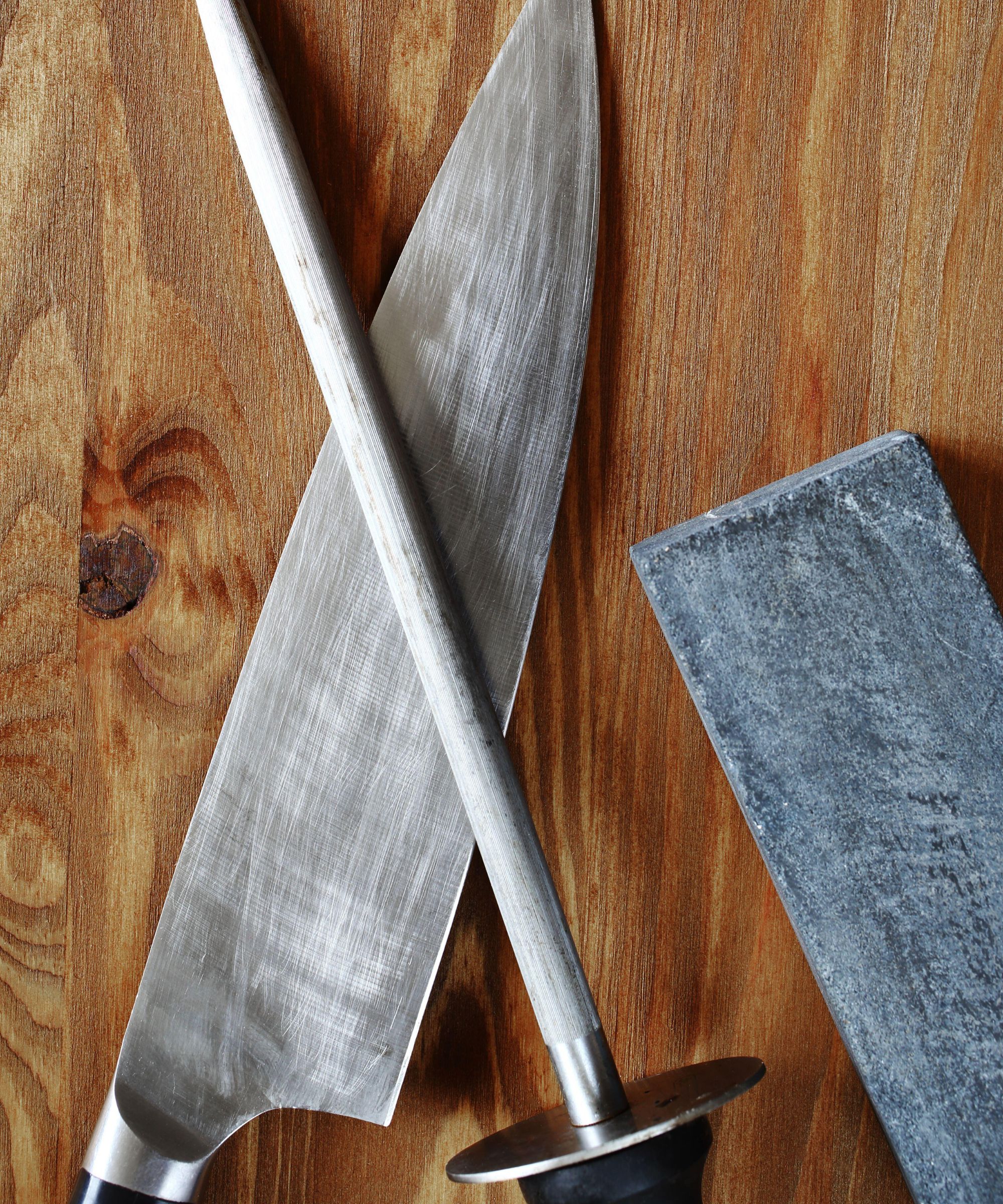 A wooden tabletop with a knife, honing rod, and whetstone