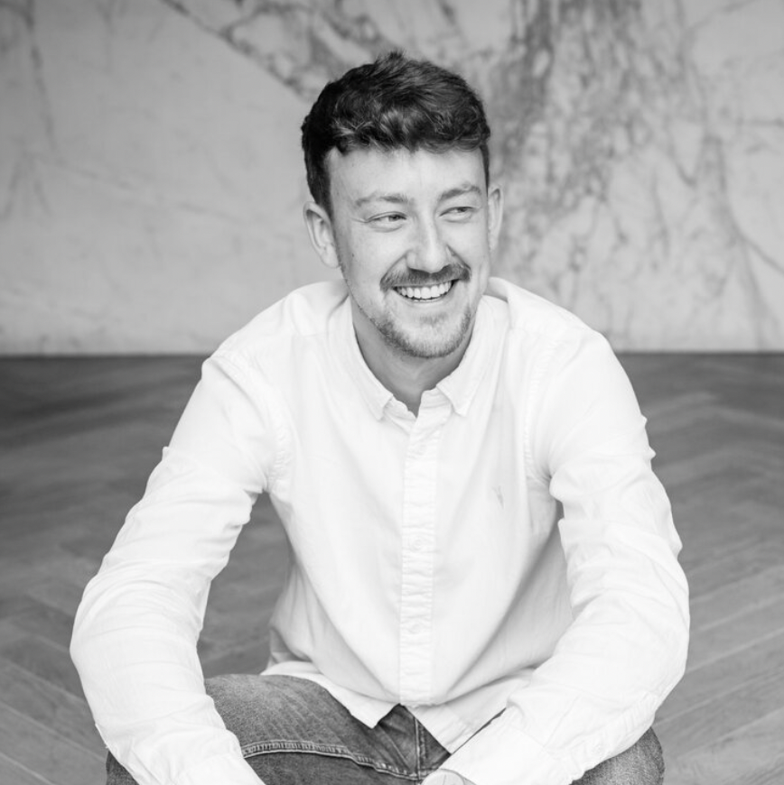 A black and white headshot of a man with dark hair in a white shirt