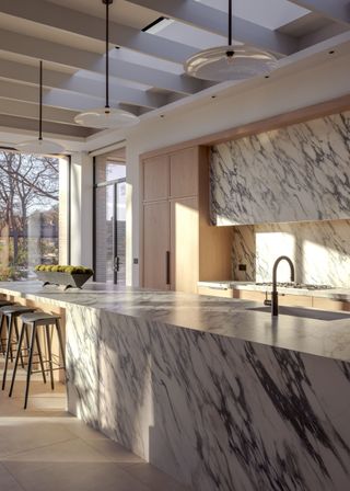 A marbles kitchen with a large island and marble backsplash that matches the island. Lighting pendants also hang above the island.