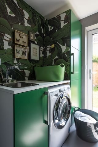 Green tropical laundry room with vibrant wallpaper and coloured cabinets