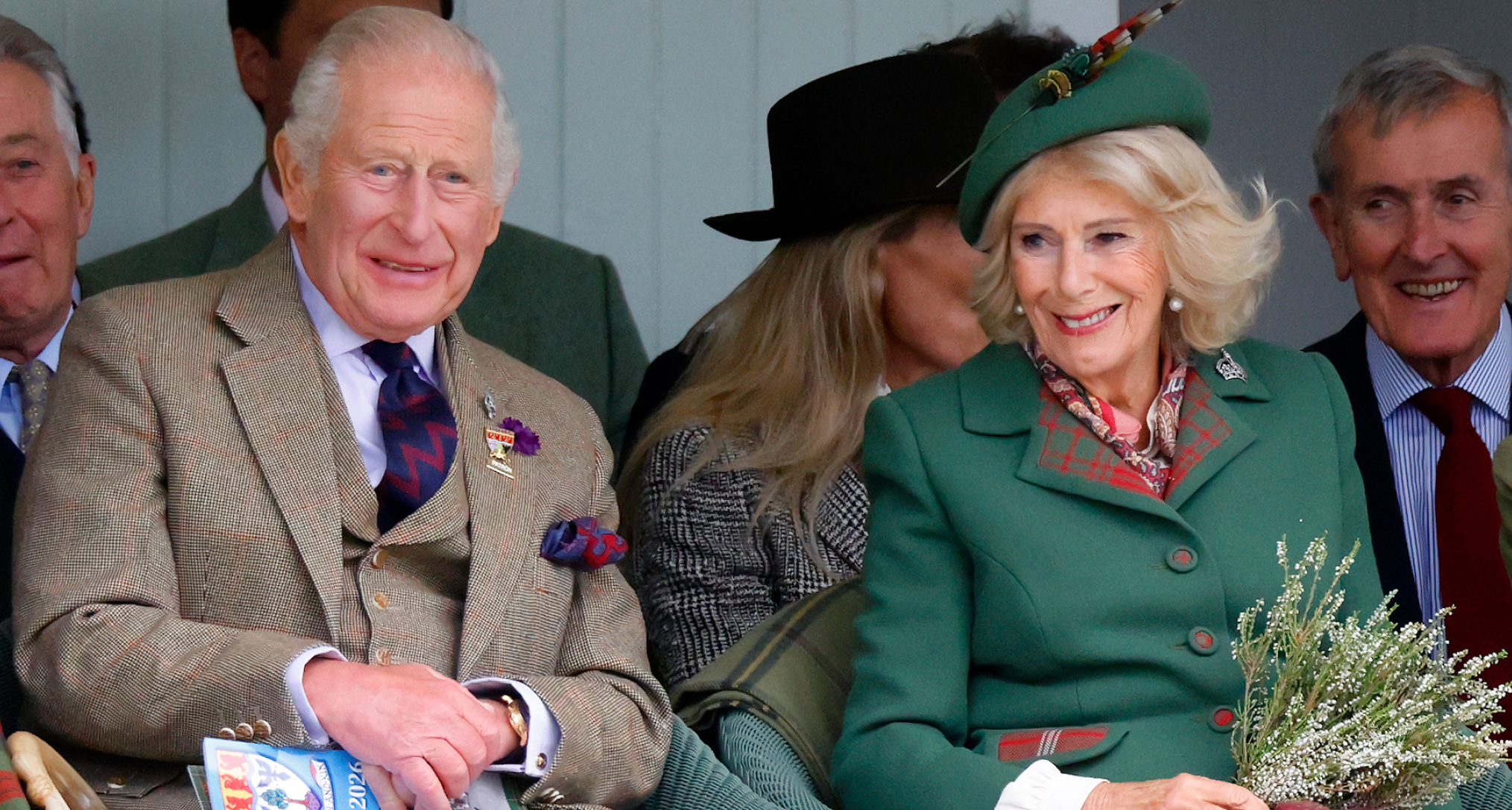 King Charles and Queen Camilla wearing tweed jackets and kilts sitting next to each other
