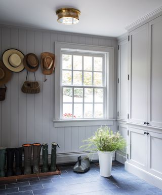 A simple mudroom with wellies storied on the floor, hats stored on coat pegs and a large window