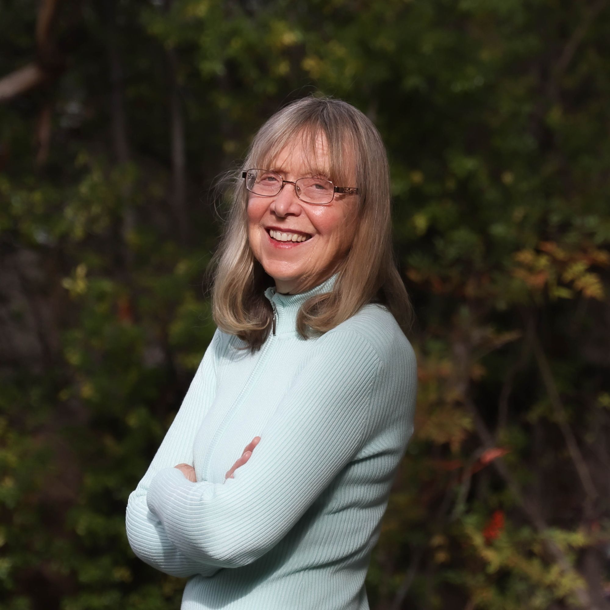 Esther Wojcicki crossing her arms while smiling and wearing glasses a light blue jumper