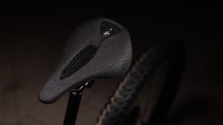 A close up of a black mesh saddle on a mountainbike in a dark studio environment