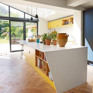 a yellow kitchen island with an overhanging surface and patio doors leading out into a garden