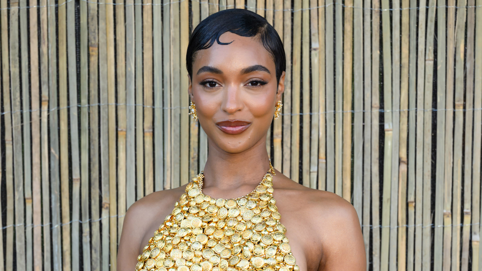 Jourdan Dunn wearing a pixie hairstyle and a gild halter neck dress.