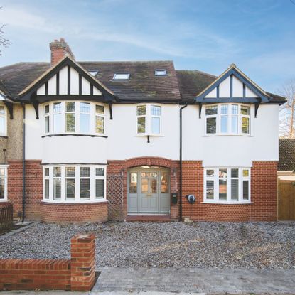 Semi-detached house with white render above and brick to the bottom of the house, with a gravel driveway in front of it