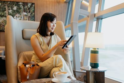 A business woman relaxes in an airport lounge with a capuccino and a tablet computer.