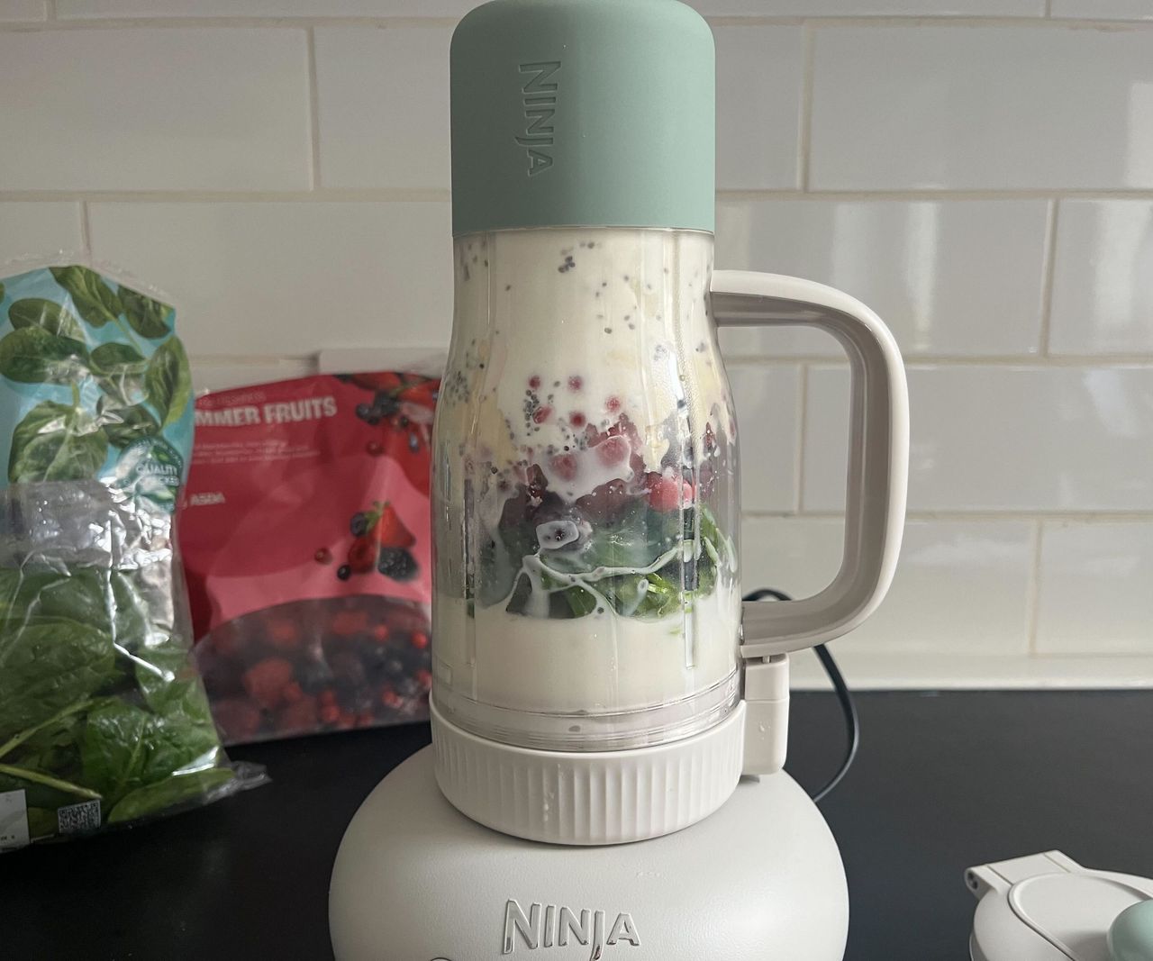 An unblended smoothie in a Ninja Blendboss tumbler in front of bags of frozen fruit and fresh spinach.
