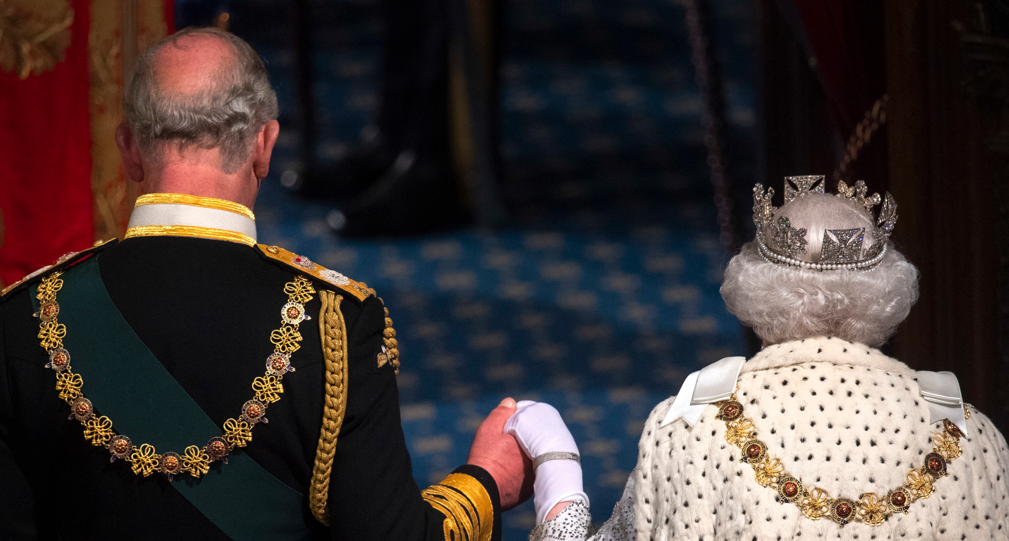 The back of Prince Charles and Queen Elizabeth holding hands and walking 