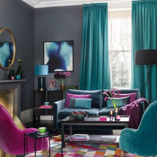 grey living room with turquoise curtains, rug with colourful triange pattern and bright pink and turquoise armchairs