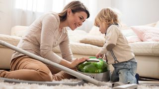 Woman and toddler looking at vacuum cleaner on a grey carpet.