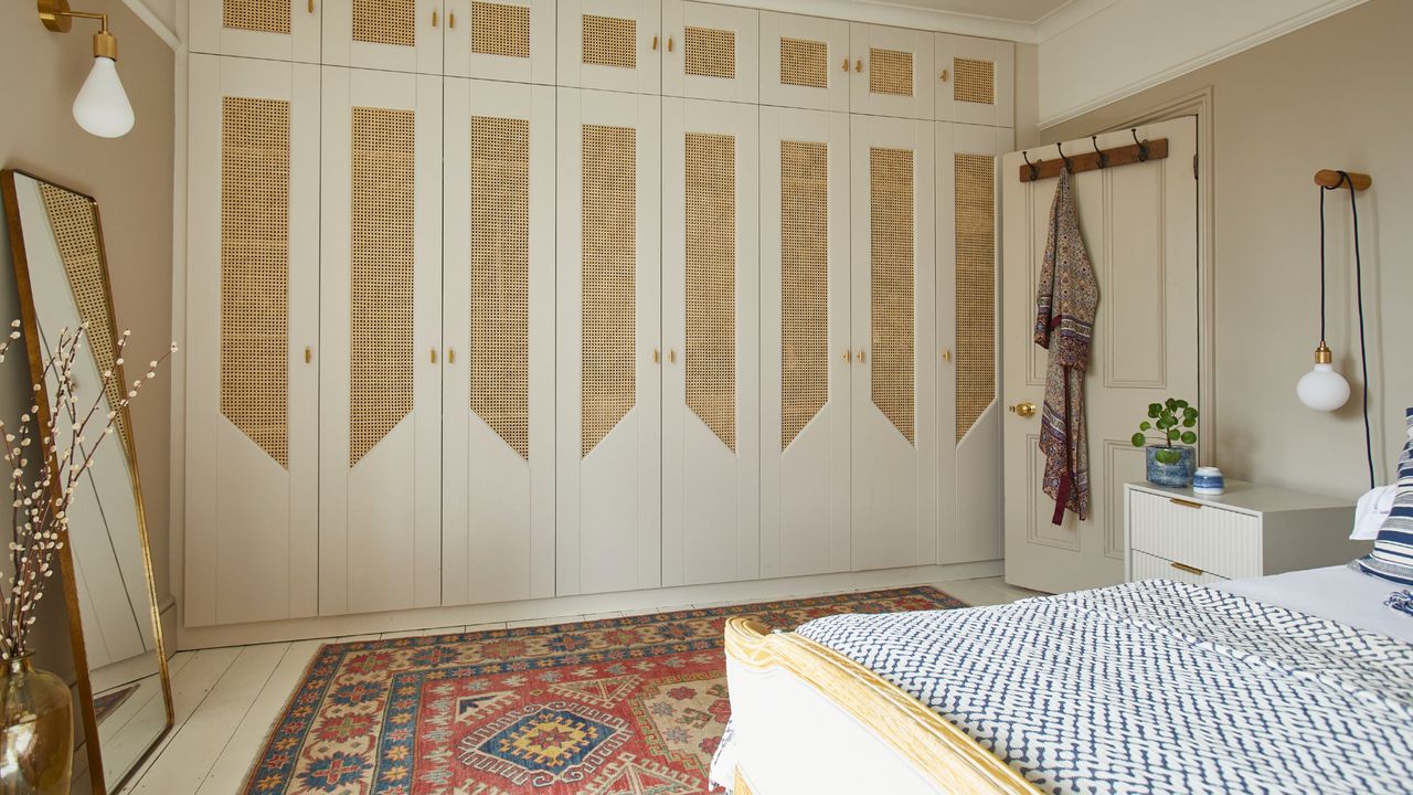 A bedroom with a colourful rug on top of white wood flooring and matching fitted wardrobes with rattan inserts