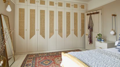 A bedroom with a colourful rug on top of white wood flooring and matching fitted wardrobes with rattan inserts