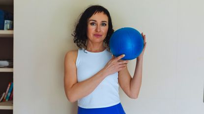 Woman holds blue Pilates ball and looks at the viewer