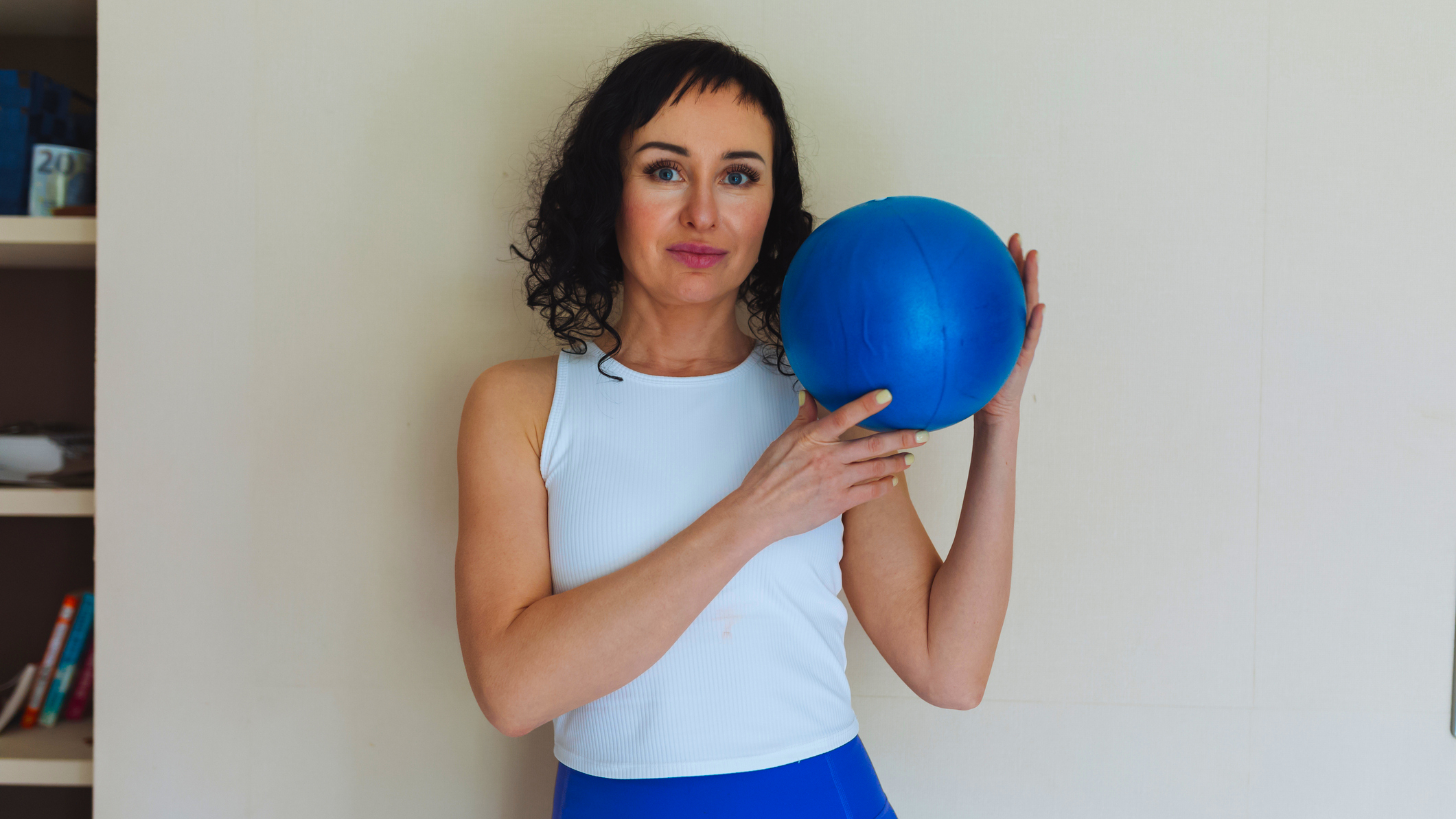 Woman holds blue Pilates ball and looks at the viewer