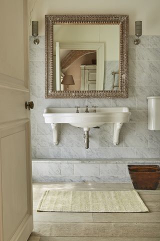 A wall-mounted bathroom sink with a large mirror, two sconce lights and a bathroom rug