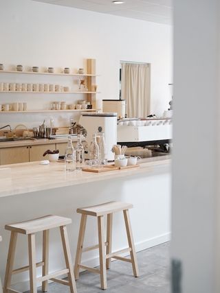 A minimalist, Scandinavian style-inspired coffee shop features a bright palette of neutrals, including white and cream, wood and plaster fixtures.