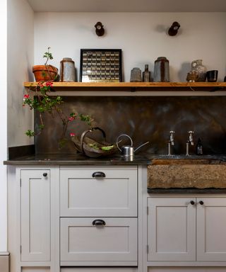 A traditional style back kitchen with greige cabinets, white walls, and a wooden shelf