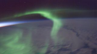 A photo of a green aurora over the night side of the earth just after sunset